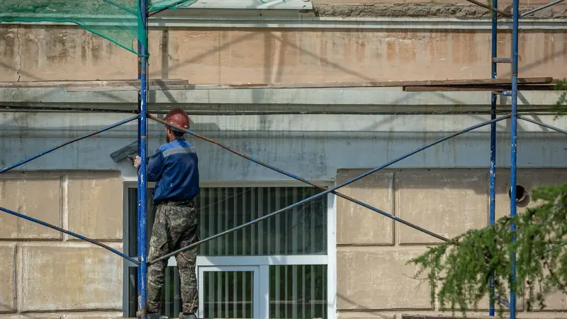Ein Handwerker arbeitet auf dem Gerüst an einer Fassade – Reverse Charge bei Bauleistungen von Subunternehmern
