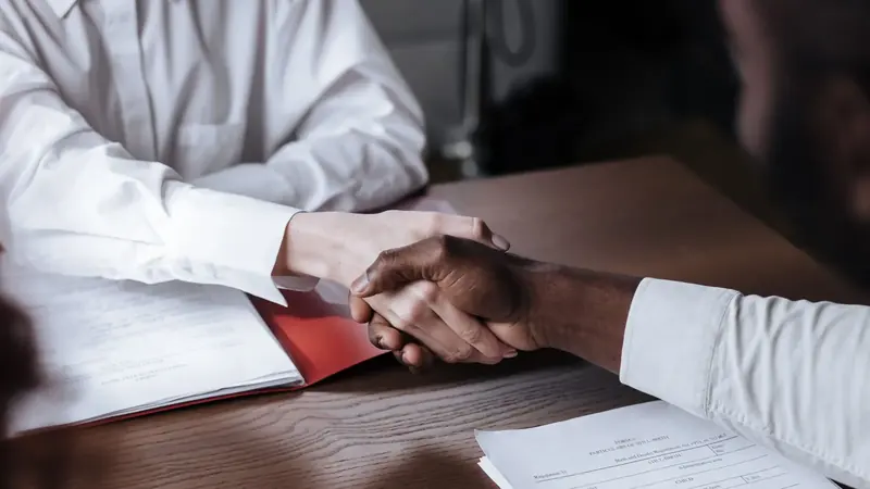Handschlag über einem Vertrag am Schreibtisch – Gesellschafterdarlehen buchen beginnt mit dem Darlehensvertrag zwischen Gesellschafter und GmbH