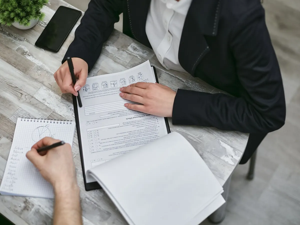 Zwei Personen am Tisch mit Unterlagen und Stift, von oben