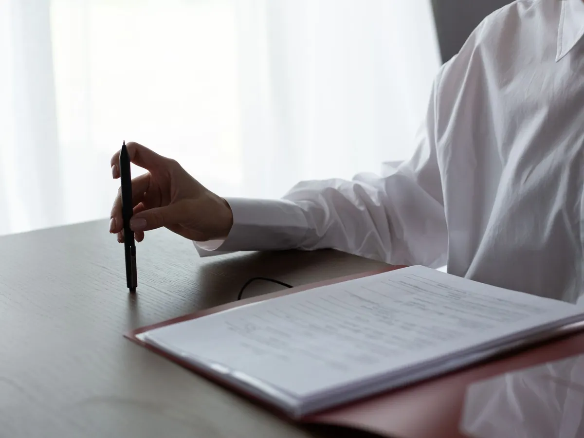 Hand mit Stift über einer Mappe mit Ausdrucken am Schreibtisch