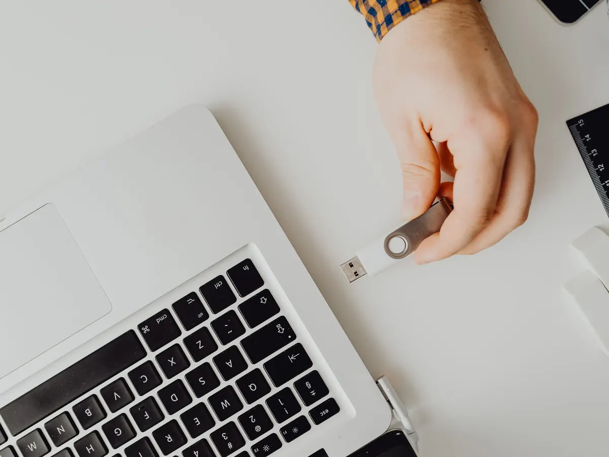 Hand hält einen USB-Stick neben einen aufgeklappten Laptop