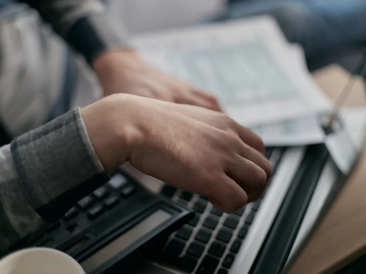 Hände tippen am Laptop neben Formularen – die Körperschaftsteuererklärung der UG mit Hauptvordruck und Anlagen