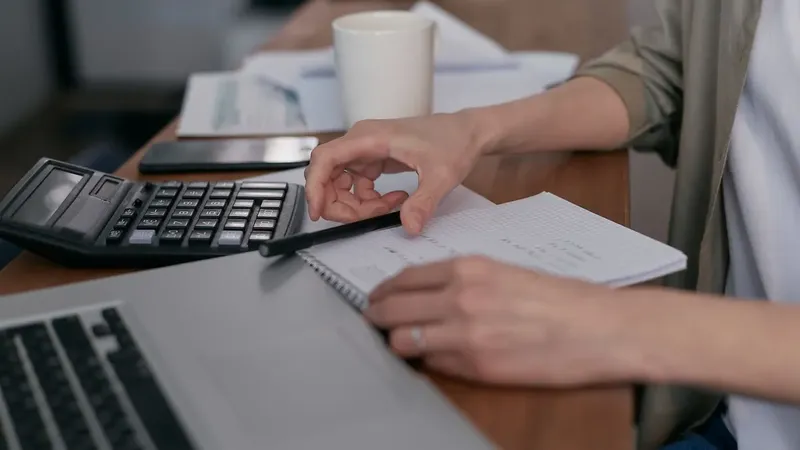 Hände mit Taschenrechner, Notizblock und Laptop – die Preise für Abschluss und Buchhaltung nachrechnen
