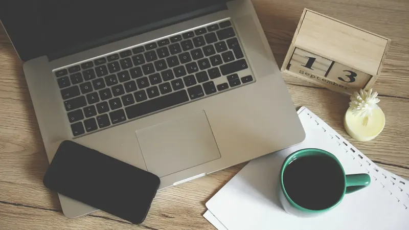 Laptop, Smartphone, Kaffee und ein Tischkalender auf dem Schreibtisch – die Buchhaltungspflichten der GmbH im Kalender