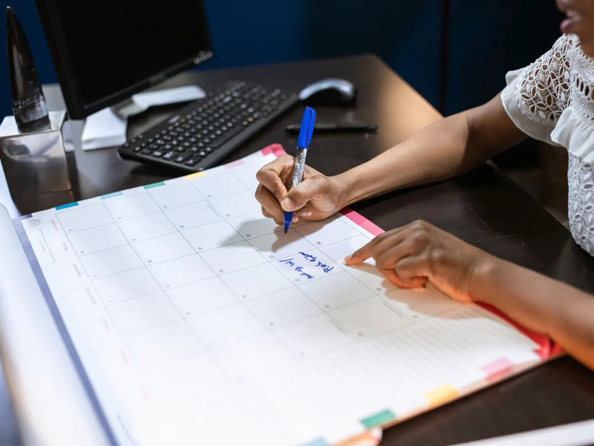 Eine Hand trägt Termine in einen großen Monatskalender auf dem Schreibtisch ein – der Monatsabschluss gehört zu den Buchhaltungspflichten der GmbH