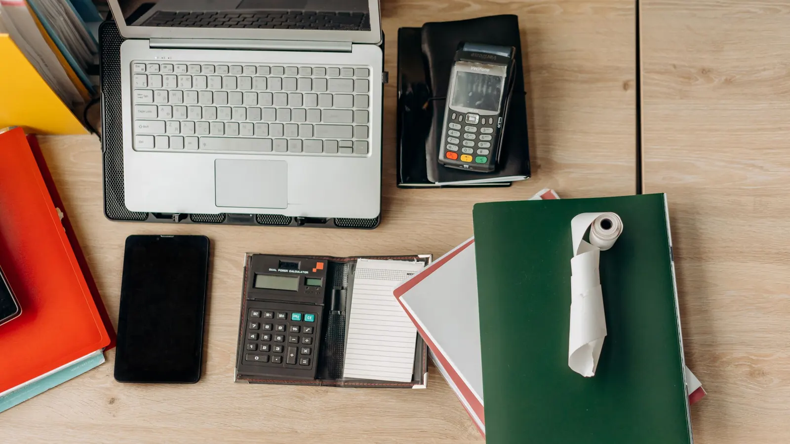 Schreibtisch von oben mit Laptop, Taschenrechner, Kartenleser und Notizbuch – Buchhaltungssoftware für GmbH und UG