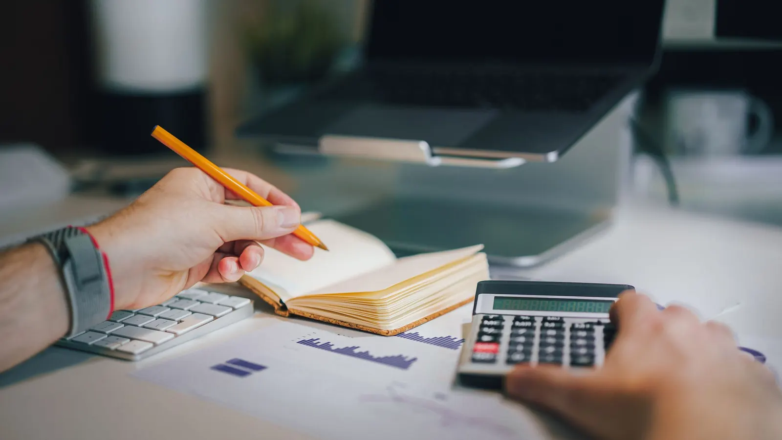 Hände mit Stift und Taschenrechner über Notizen und Diagrammen – Verlustvortrag der GmbH vom Verlustjahr ins Gewinnjahr