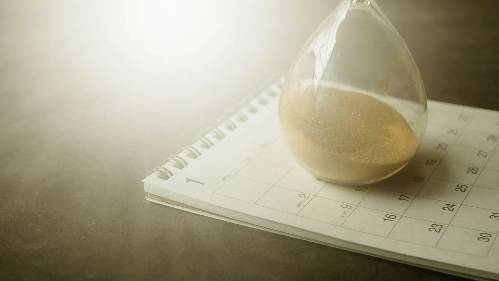 Eine Sanduhr steht auf einem Kalender – eine Frist läuft ab
