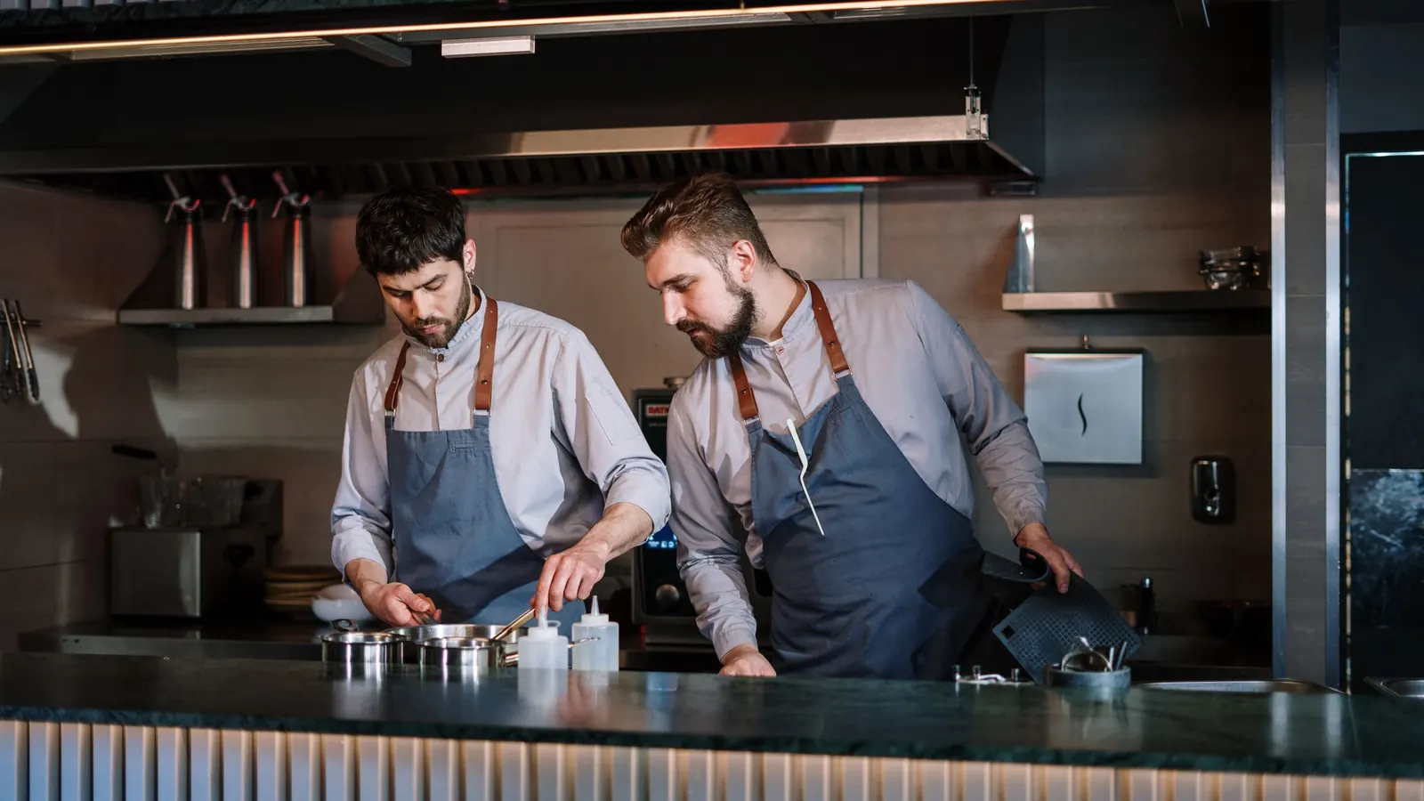 Zwei Köche in Schürzen bereiten in einer offenen Restaurantküche Essen zu