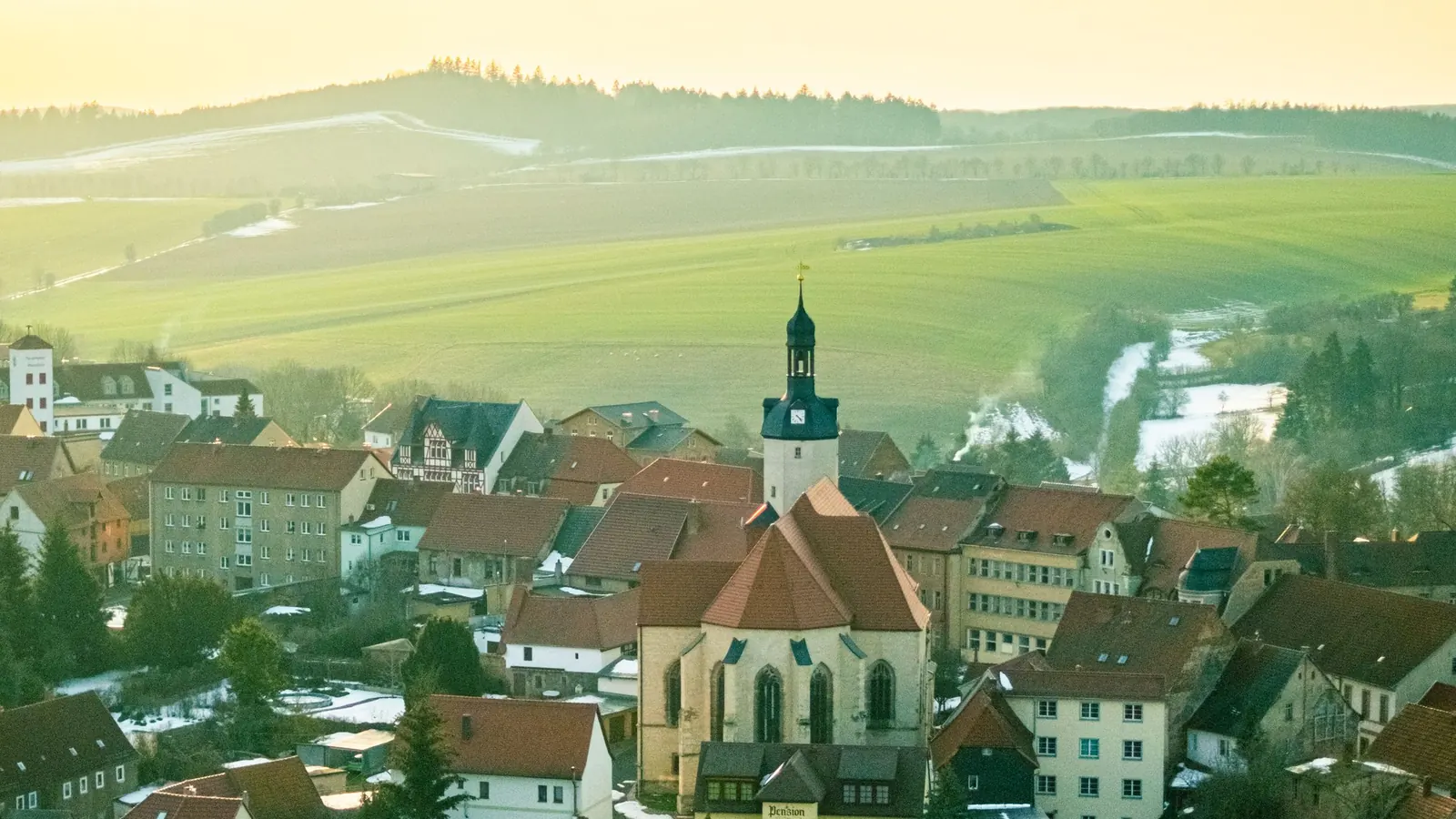 Eine kleine Stadt mit Kirche zwischen Feldern und Hügeln – Gewerbesteuer-Hebesätze im Land