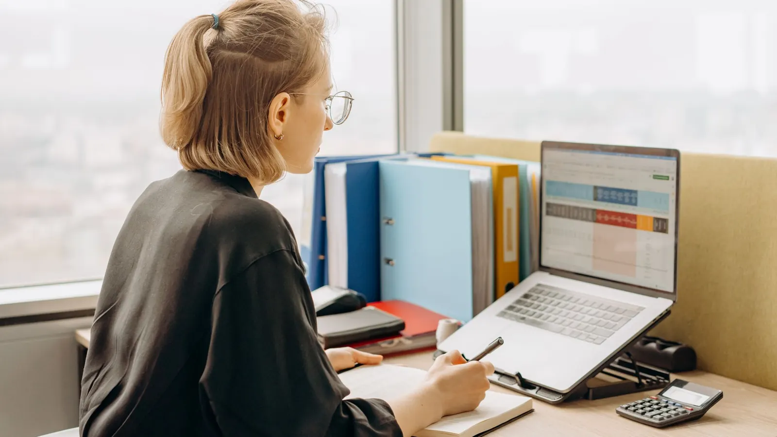 Eine Frau arbeitet am Laptop mit Tabellen, daneben Unterlagen