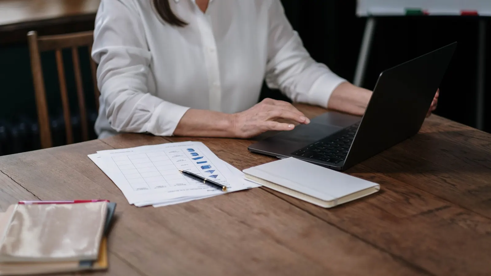 Eine Unternehmerin arbeitet am Laptop, daneben Unterlagen und ein Notizbuch