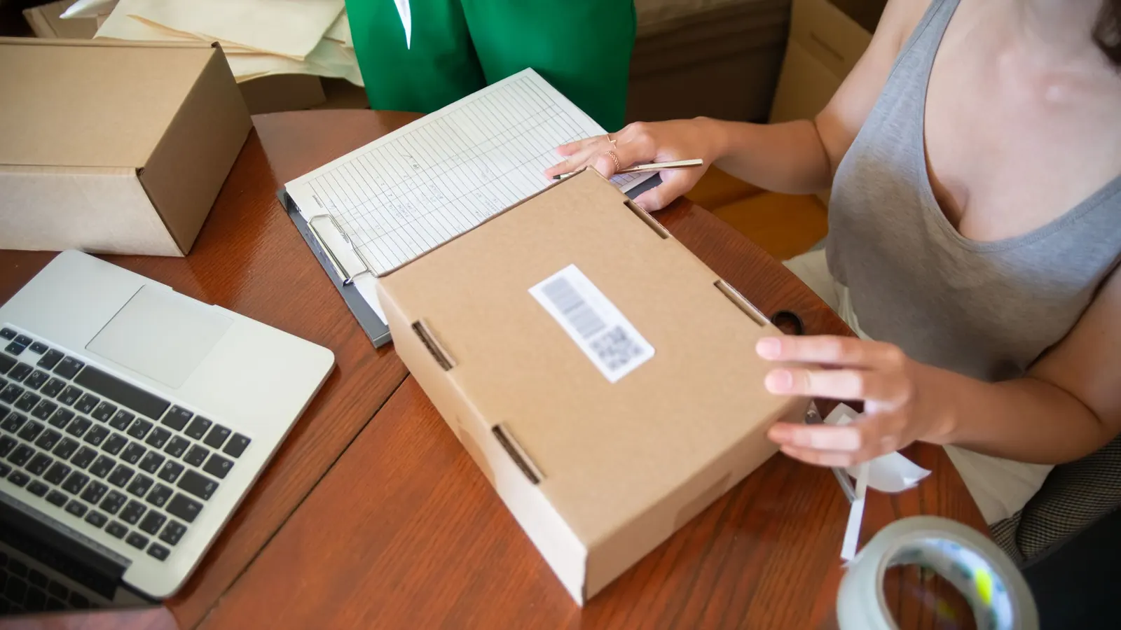 Zwei Menschen packen Bestellungen aus dem Onlinehandel am Laptop in Kartons
